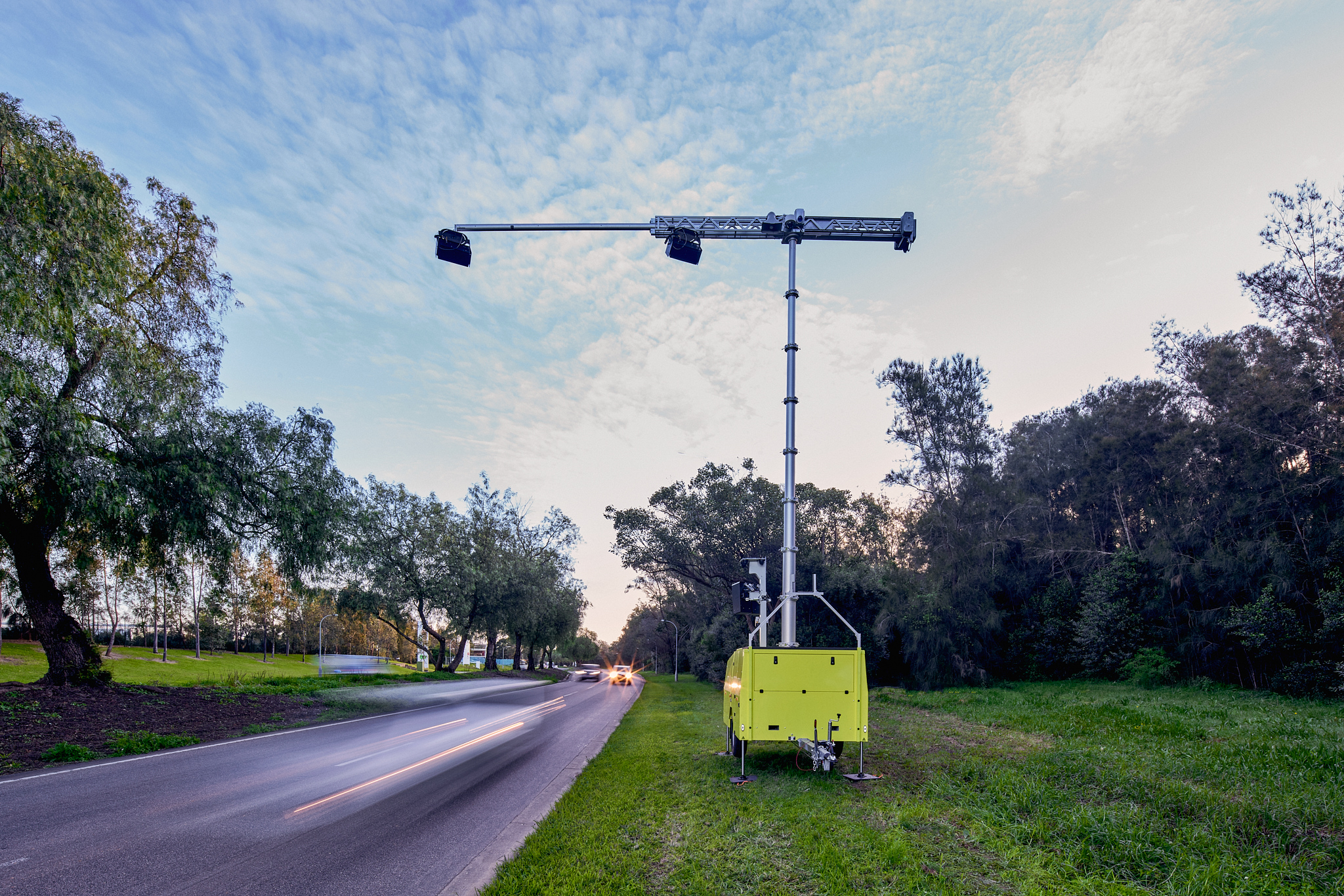 A mobile roadside camera rig mounted on a trailer beside a tree-lined road.
