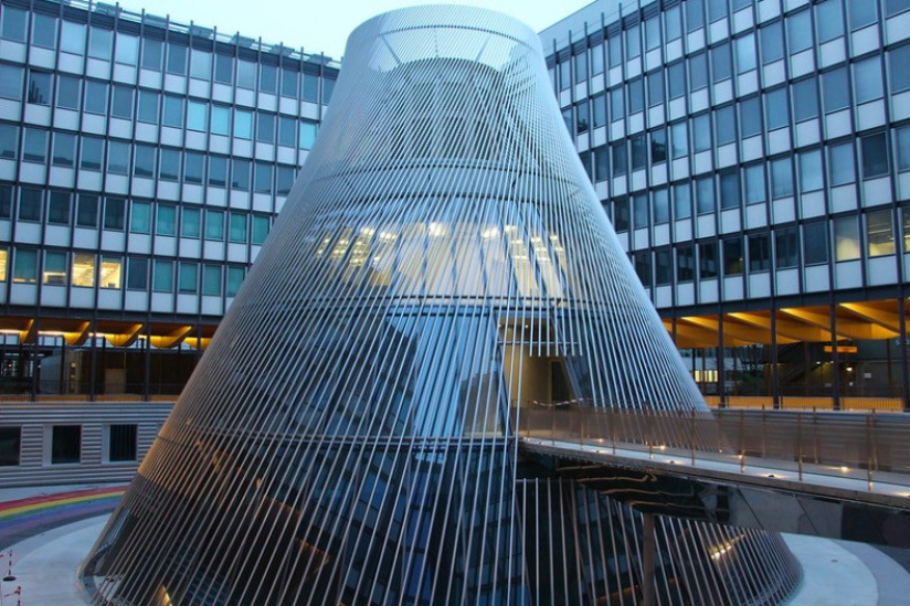 A metal sculpture rising through a courtyard surrounded by glass fronted buildings.